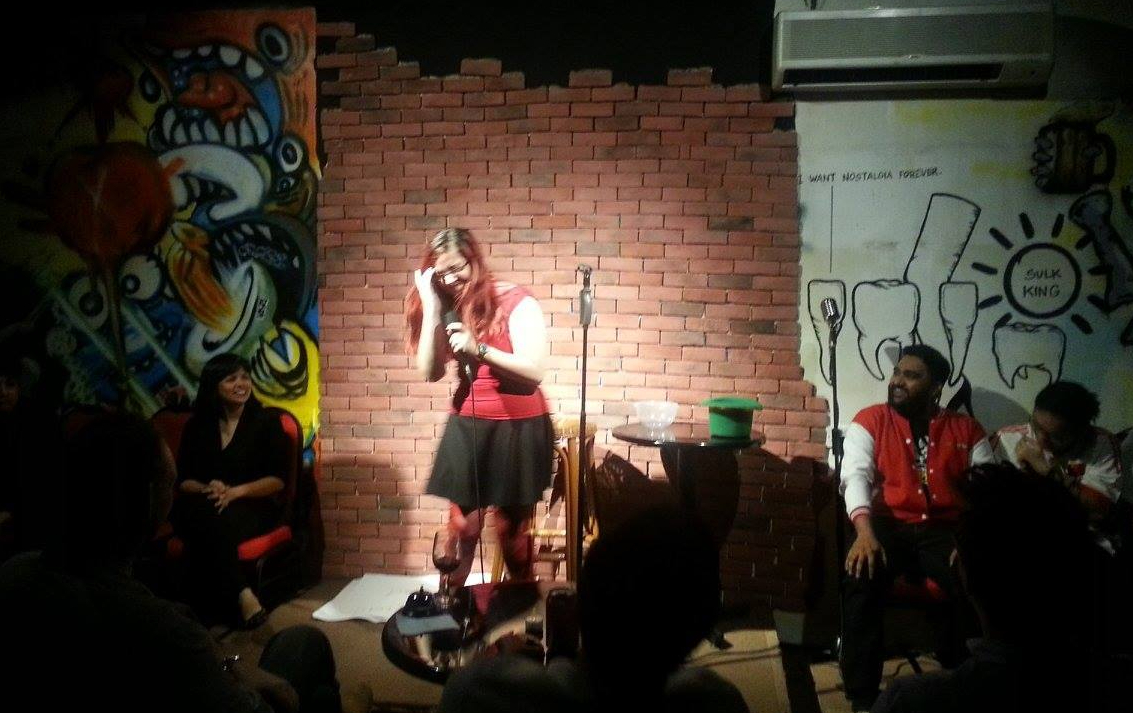 Dominica May laughing on stage in front of a brick wall as she performs as part of Hack the Crack at Crackhouse Comedy Club.